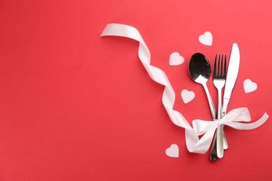 Photo of Beautiful cutlery set, hearts and white bow on red background, flat lay with space for text. Valentine's Day dinner