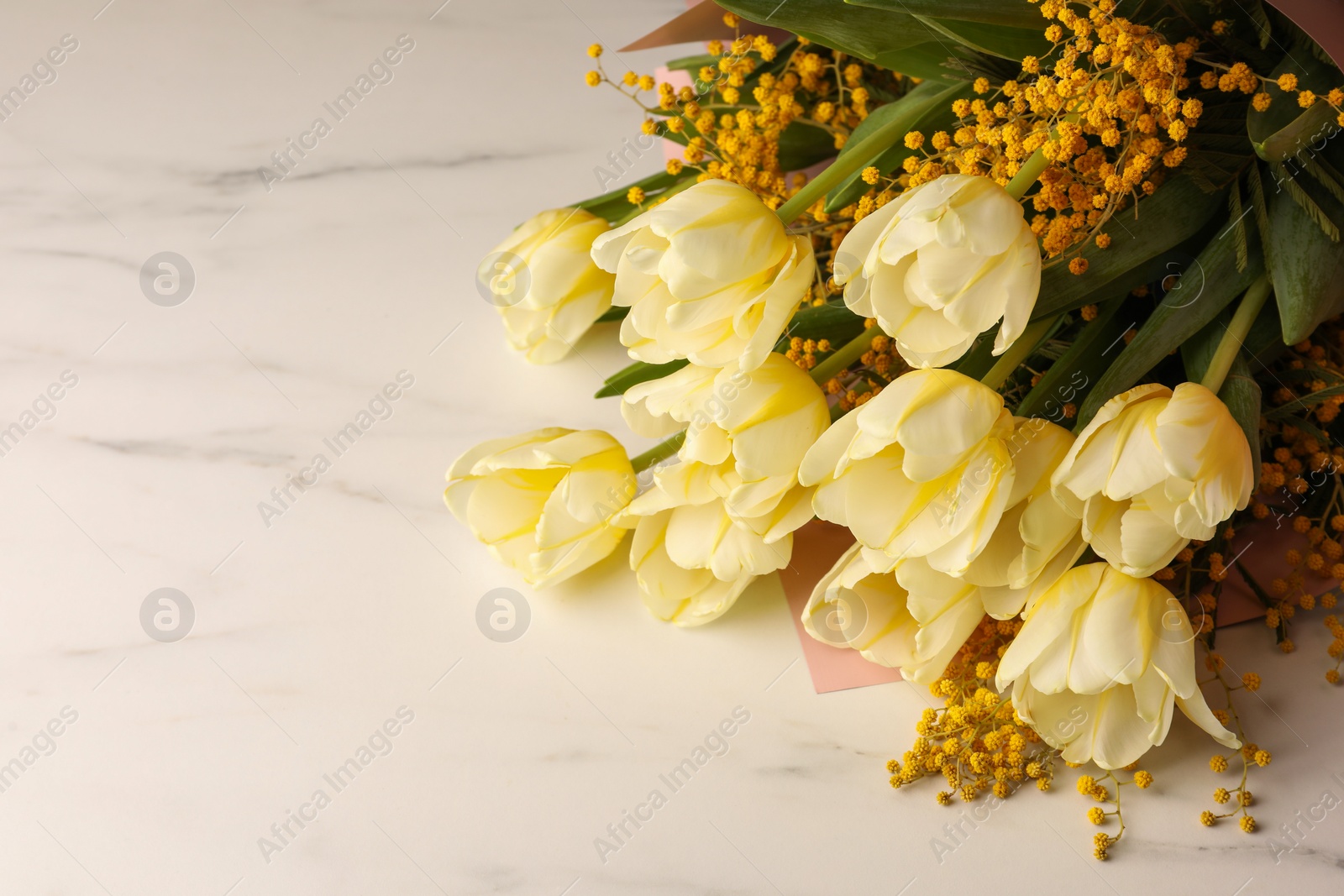 Photo of Bouquet with beautiful tulips and mimosa flowers on white marble table. Space for text