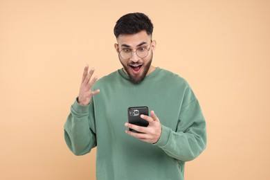 Photo of Emotional young man using smartphone on beige background