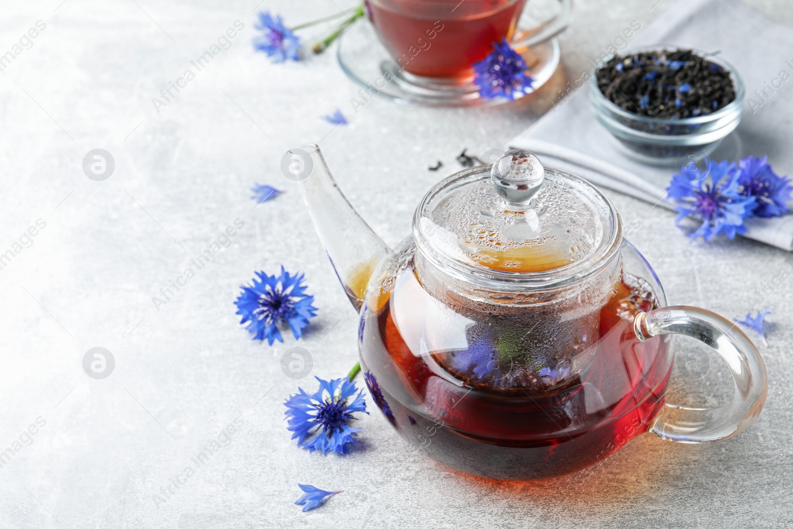 Photo of Glass pot with tea and cornflowers on light table. Space for text