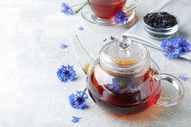 Photo of Glass pot with tea and cornflowers on light table. Space for text