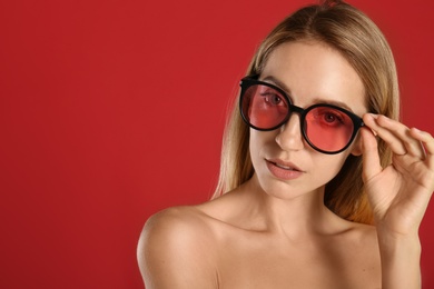 Beautiful woman in stylish sunglasses on red background. Space for text