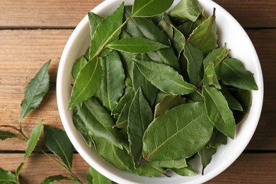 Aromatic fresh bay leaves and bowl on wooden table, top view