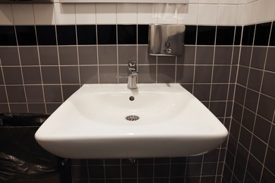 Photo of Public toilet interior with sink and tiled wall