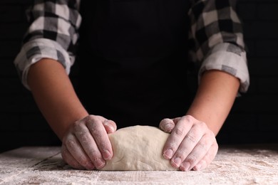 Photo of Man kneading dough at wooden table on dark background, closeup