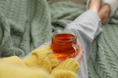 Woman with cup of tea sitting on plaid, closeup