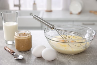 Whisk, bowl, beaten eggs and other ingredients on grey table indoors