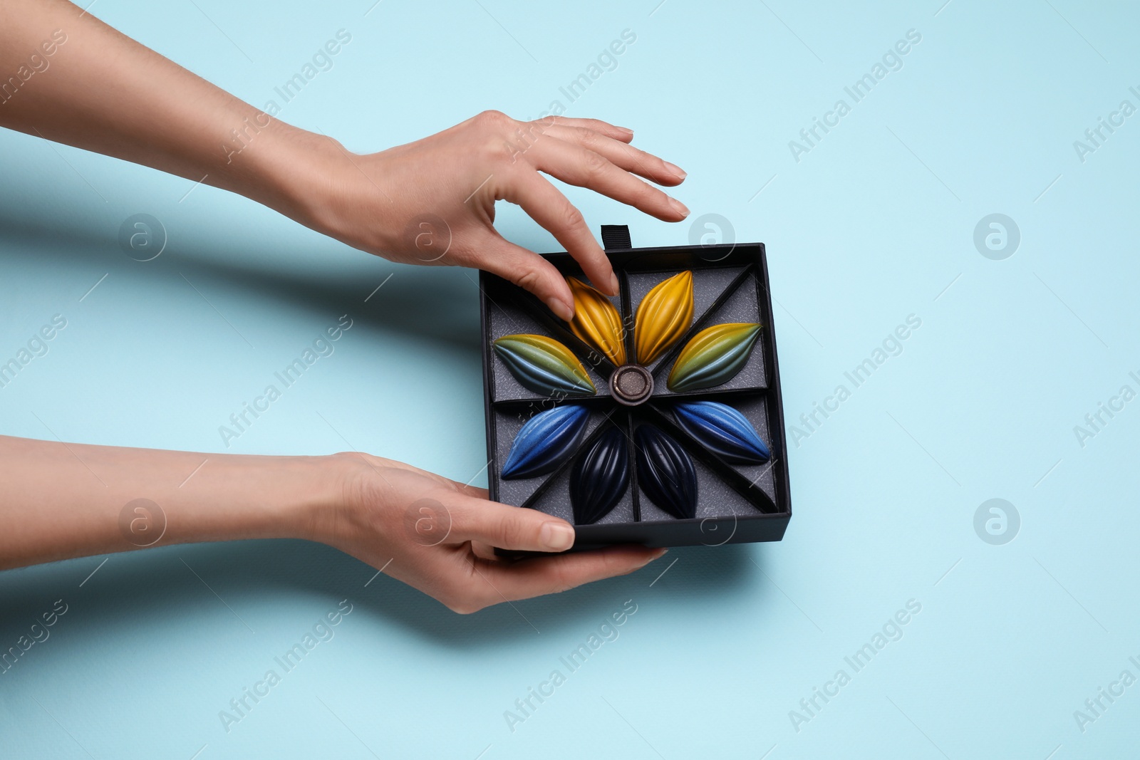 Photo of Woman with box of delicious chocolate candies on light blue background, top view