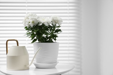 Photo of Beautiful chrysanthemum plant in flower pot and watering can on white table indoors, space for text