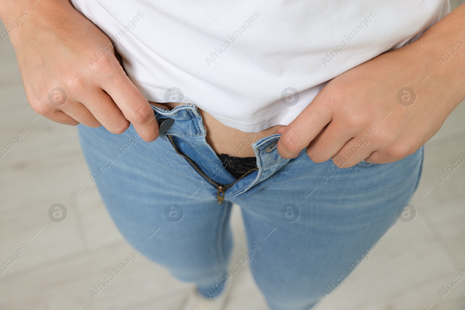 Photo of Woman trying to put on tight jeans indoors, closeup