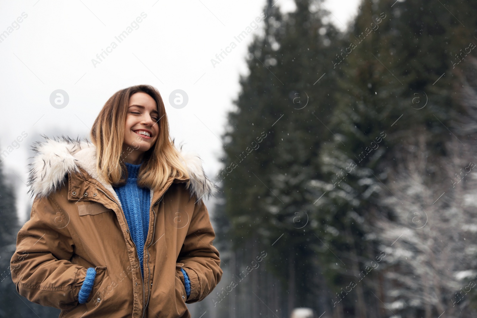 Photo of Young woman in warm clothes near forest, space for text. Winter vacation