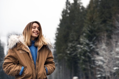 Photo of Young woman in warm clothes near forest, space for text. Winter vacation