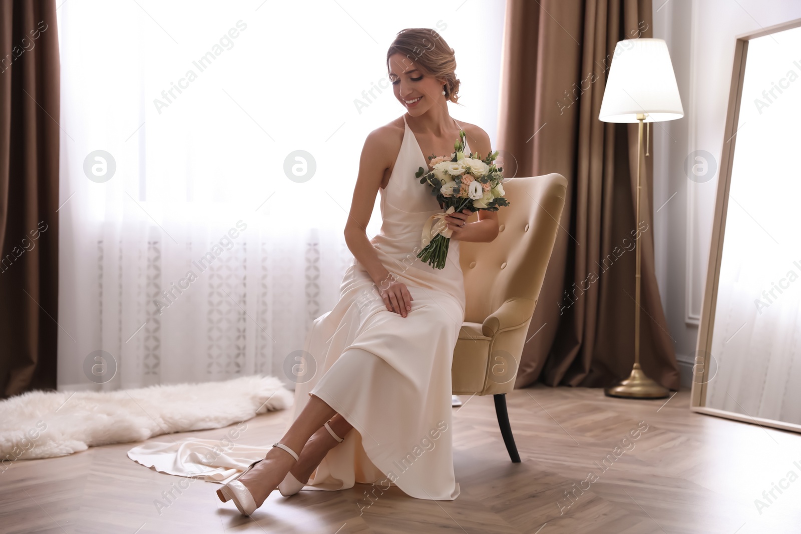 Photo of Beautiful young bride in elegant wedding dress with bouquet sitting in armchair