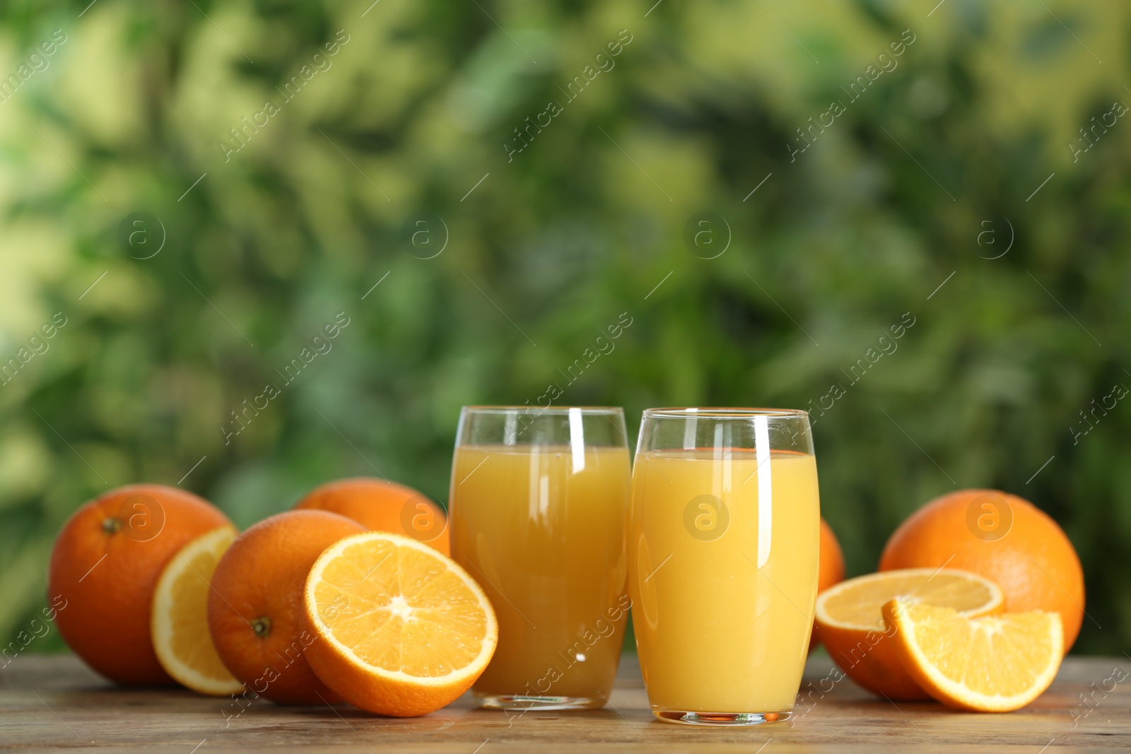 Photo of Delicious orange juice and fresh fruits on wooden table against blurred background. Space for text