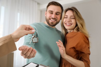 Photo of Real estate agent giving key to happy young couple in new house, focus on hands