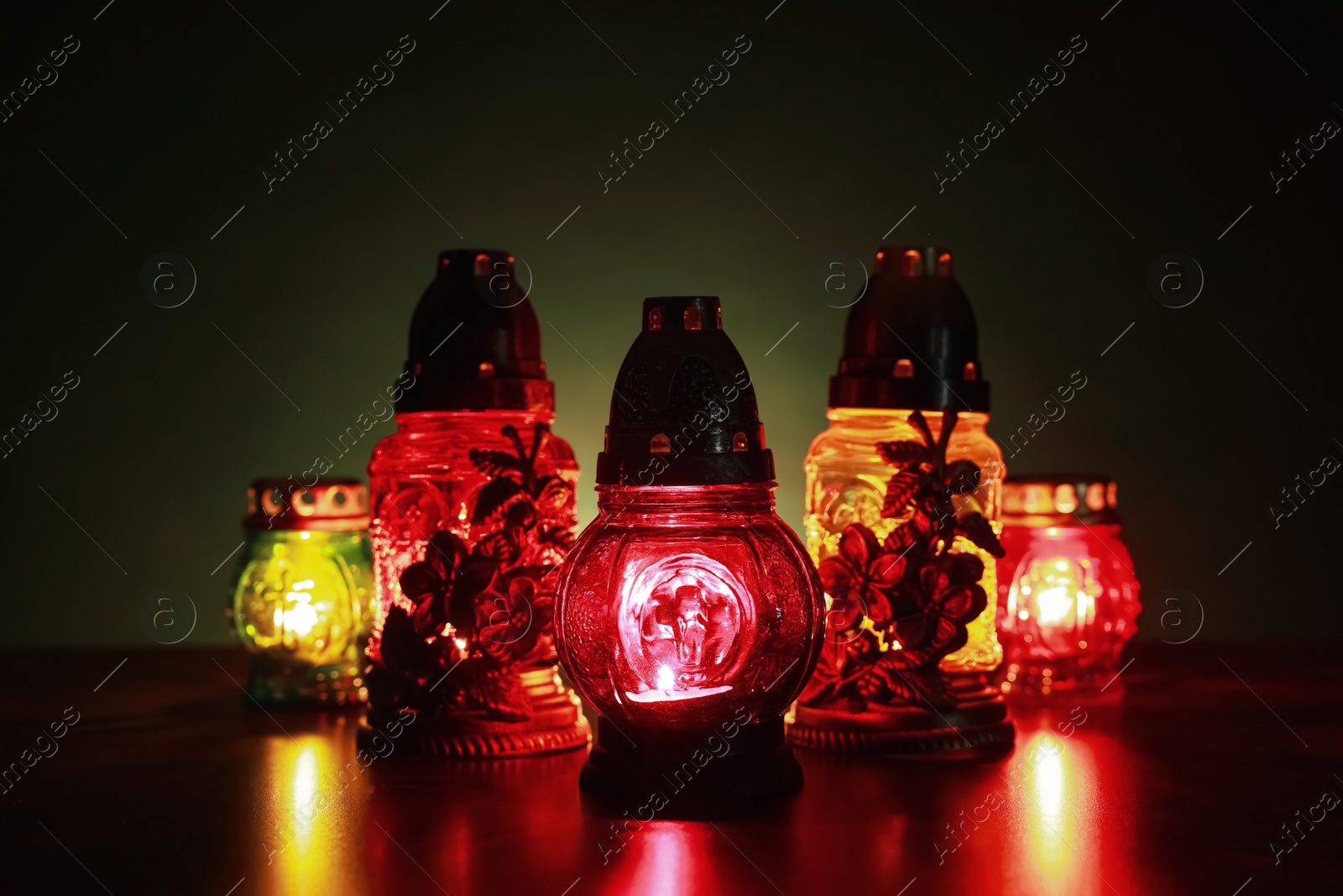 Photo of Beautiful glowing grave lights on table in darkness. Symbol of remembrance