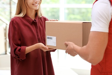 Photo of Young woman receiving parcel from courier indoors. Delivery service