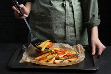 Cooker near baking pan with tasty parsnip and bell pepper at dark grey table, closeup