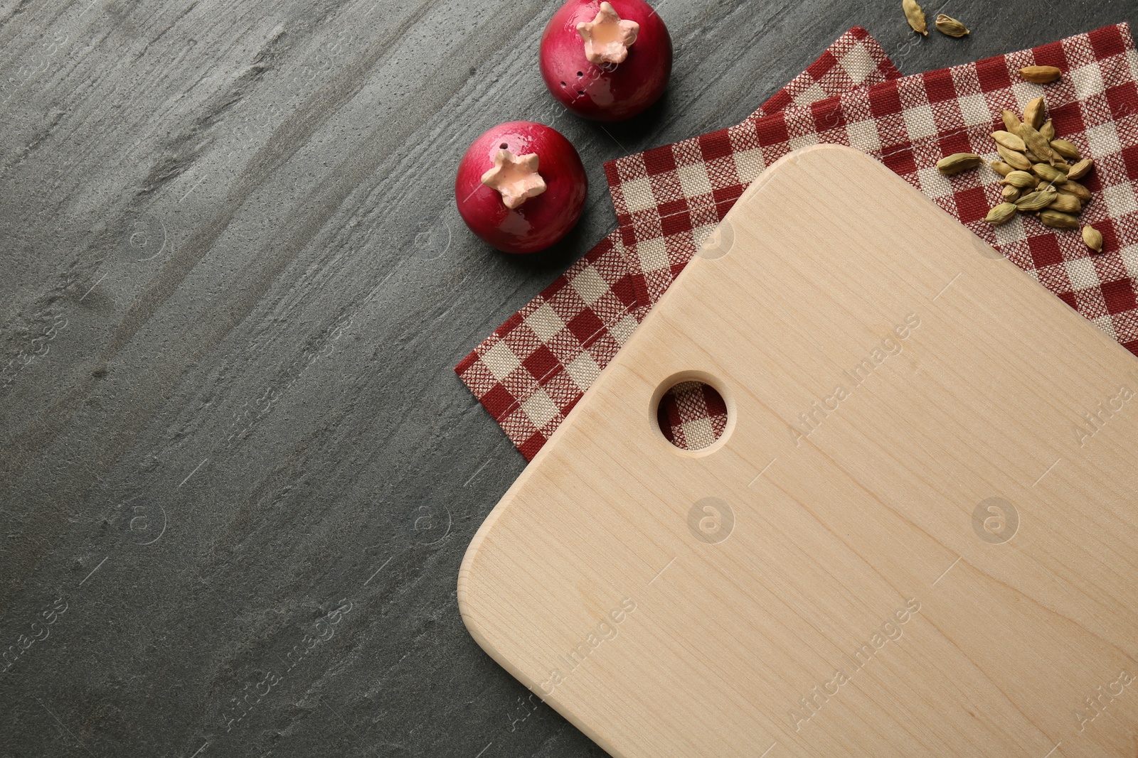 Photo of Wooden cutting board, kitchen towel and cardamom pods on dark grey table, flat lay. Space for text