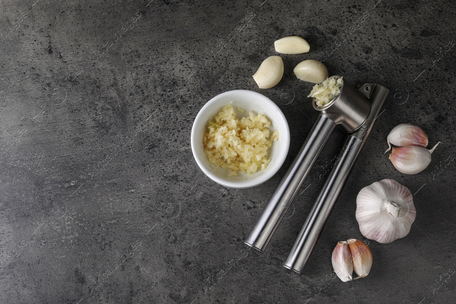 Photo of Garlic press, cloves and mince on grey table, flat lay. Space for text