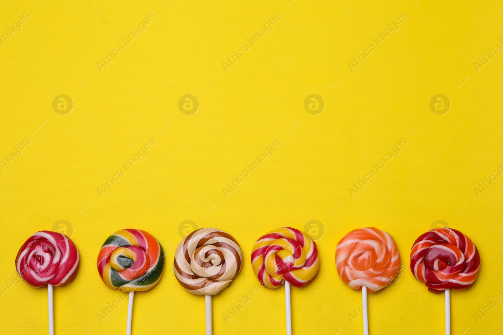 Photo of Delicious lollipops on yellow background, flat lay. Space for text