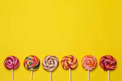 Delicious lollipops on yellow background, flat lay. Space for text