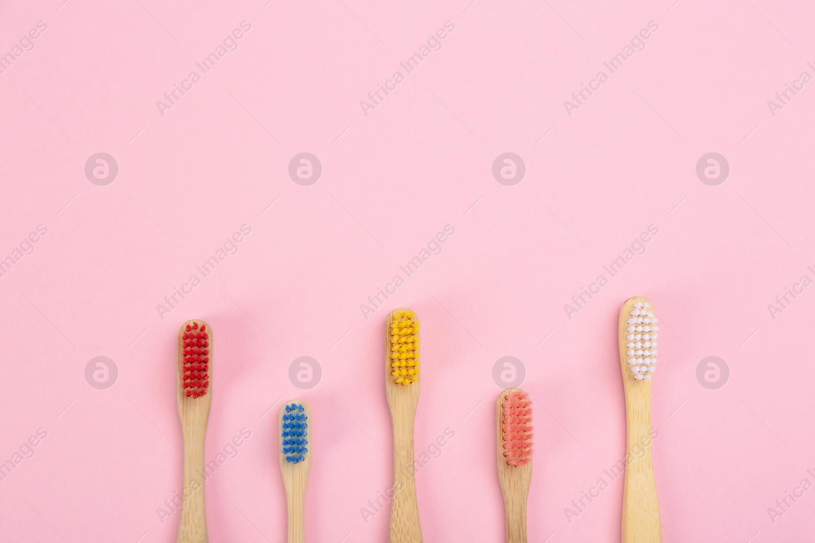 Photo of Toothbrushes made of bamboo on pink background, flat lay. Space for text