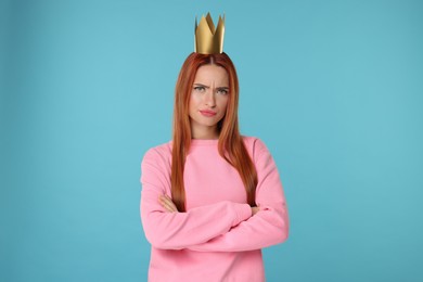 Emotional young woman with princess crown on light blue background