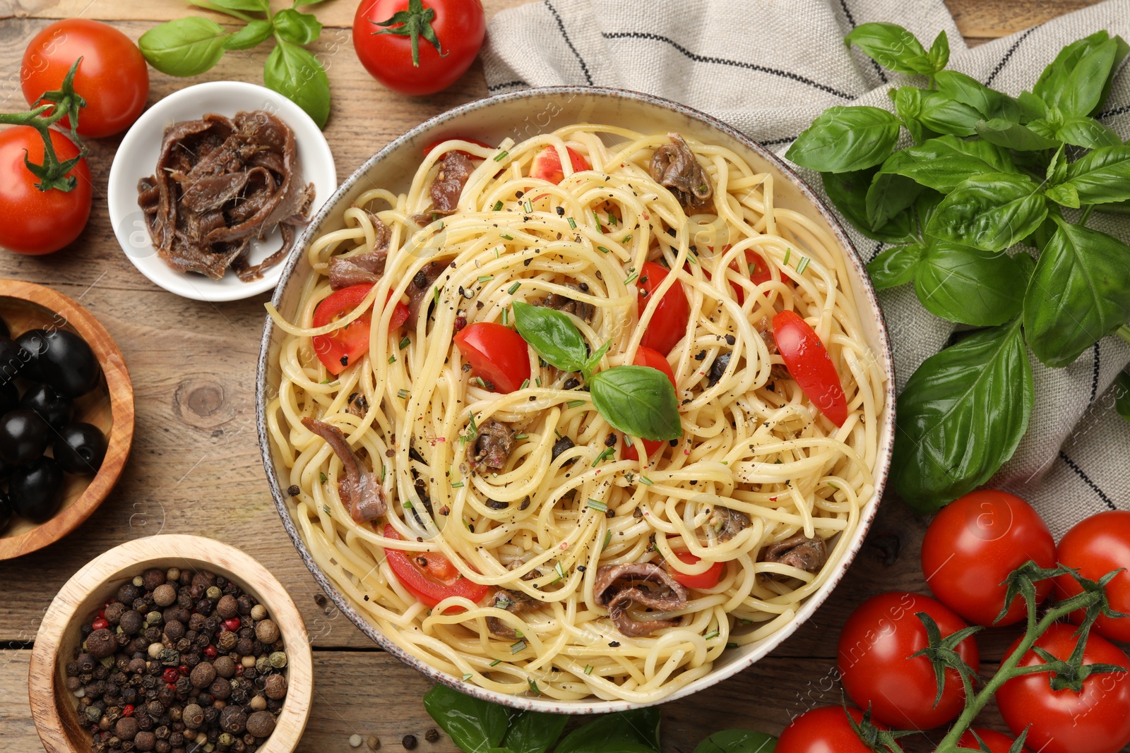 Photo of Delicious pasta with anchovies, tomatoes and spices on wooden table, flat lay