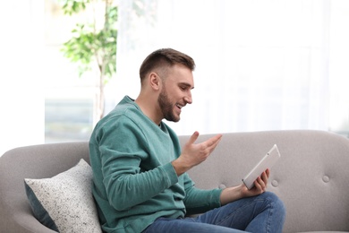 Photo of Young man using video chat on tablet in living room