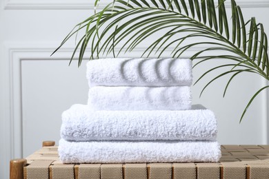 Photo of Stacked terry towels and green leaf on wicker bench indoors