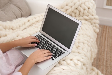 Woman using laptop on couch with soft knitted blanket at home, closeup