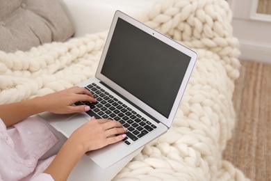 Photo of Woman using laptop on couch with soft knitted blanket at home, closeup