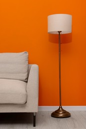Photo of Comfortable sofa and stylish lamp near orange wall indoors