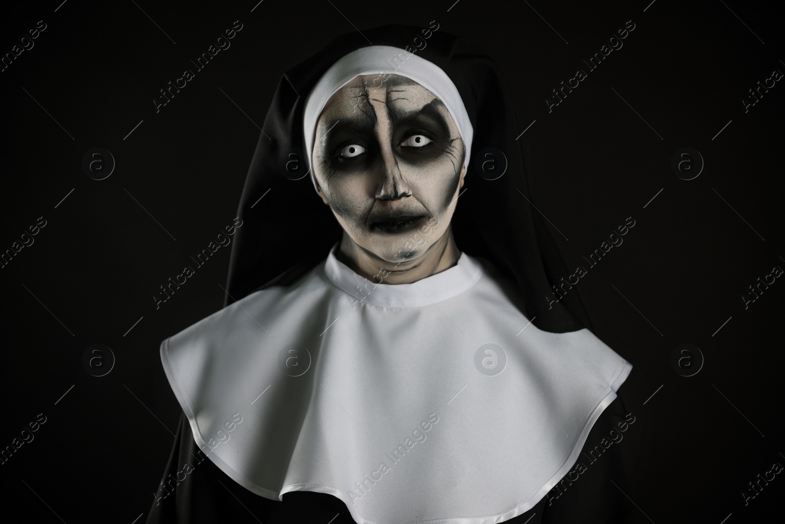 Photo of Portrait of scary devilish nun on black background. Halloween party look