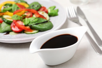 Photo of Balsamic vinegar in gravy boat near plate with vegetable salad on table, closeup