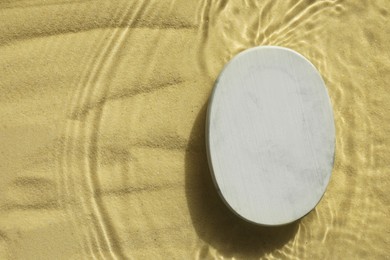 Photo of Stylish presentation for product. Stone podium in water on sand, top view. Space for text