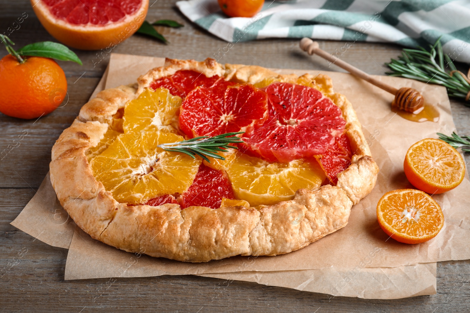 Photo of Delicious galette with citrus fruits and rosemary on wooden table