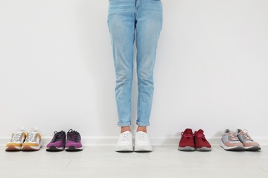 Photo of Woman trying on different shoes near white wall, closeup