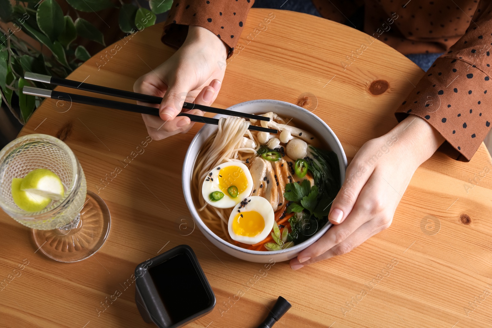 Photo of Woman eating delicious ramen with chopsticks at wooden table, above view. Noodle soup