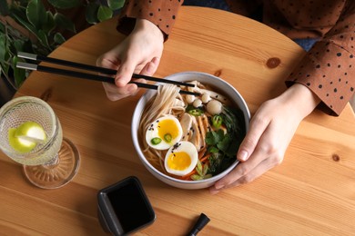 Woman eating delicious ramen with chopsticks at wooden table, above view. Noodle soup