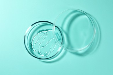 Photo of Petri dish with liquid and lid on turquoise background, top view