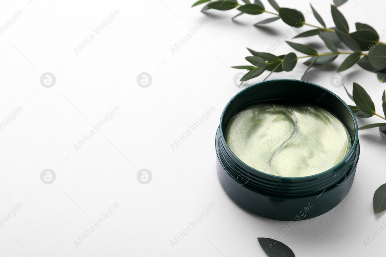 Photo of Under eye patches in jar near green twigs on white background. Space for text