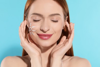 Photo of Beautiful young woman with sun protection cream on her face against light blue background