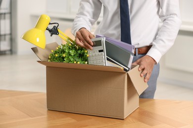 Photo of Unemployment problem. Man with box of personal belongings at table in office, closeup