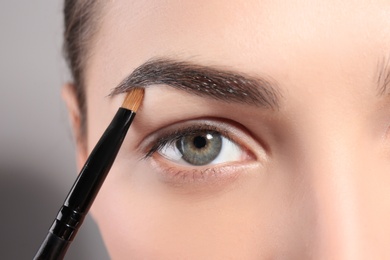 Photo of Young woman correcting eyebrow shape with brush, closeup