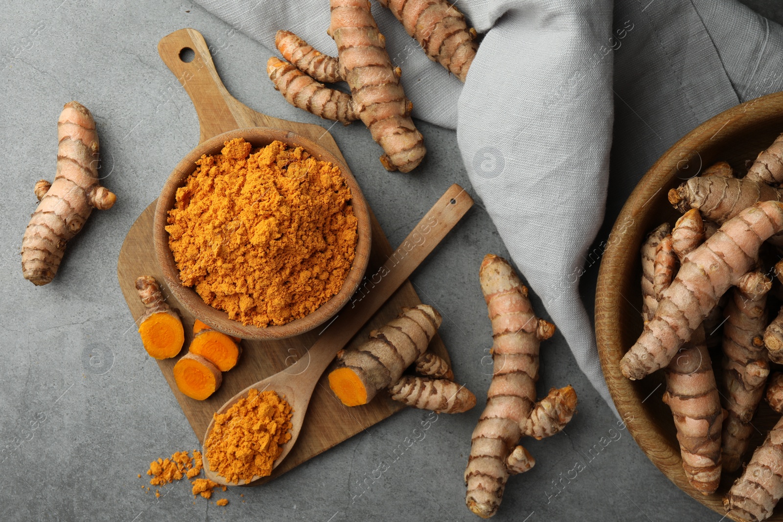 Photo of Aromatic turmeric powder and raw roots on grey table, flat lay