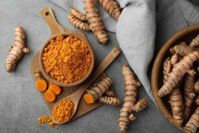 Aromatic turmeric powder and raw roots on grey table, flat lay