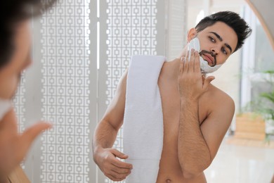 Photo of Handsome young man applying shaving foam near mirror in bathroom