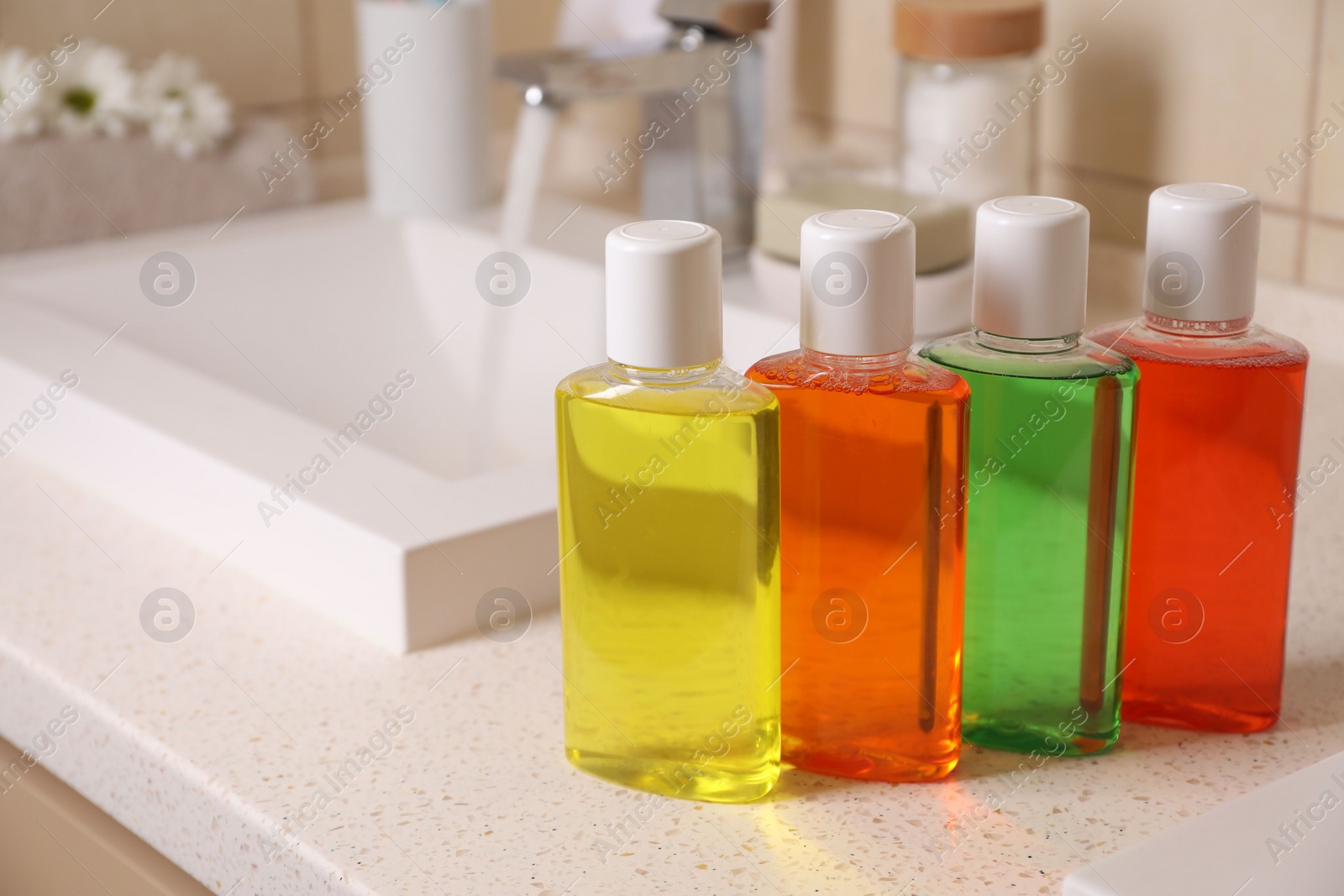 Photo of Fresh mouthwashes in bottles on countertop near sink, closeup. Space for text